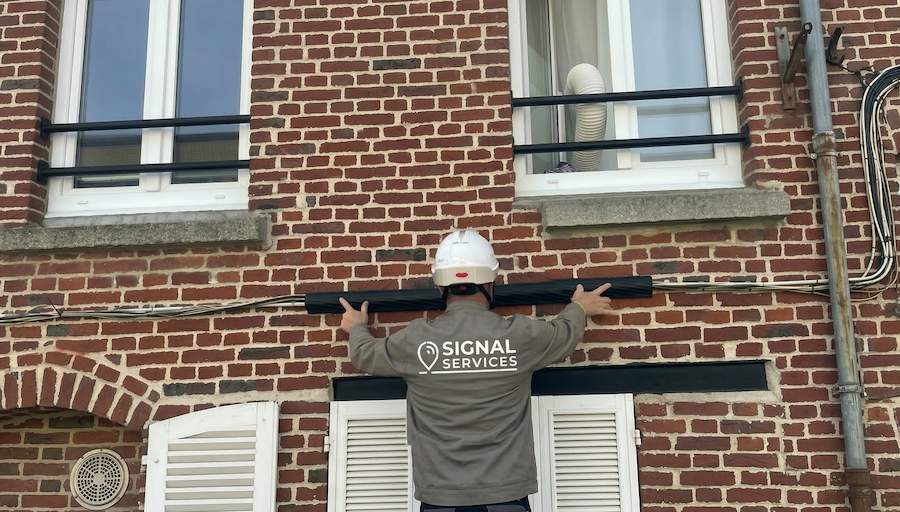 Technicien Signal Services en train de poser un système de câches-cables sur une façade